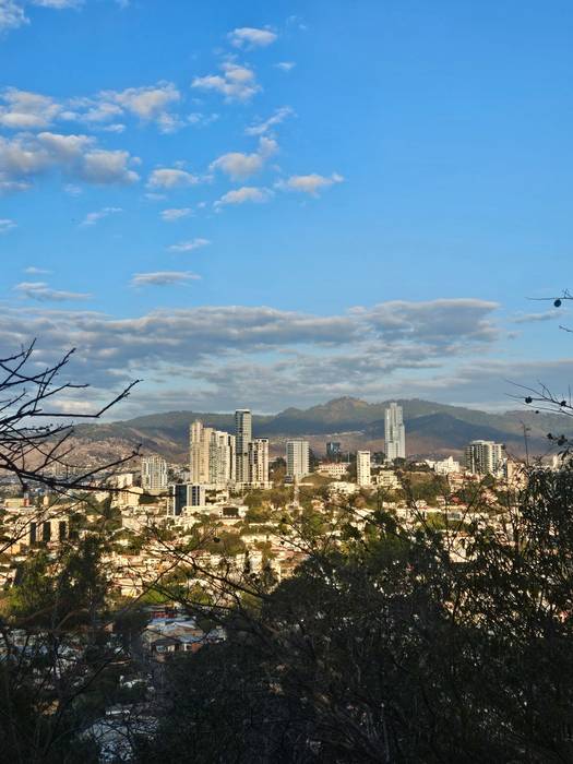 A city spread out below a hillside under afternoon clouds
